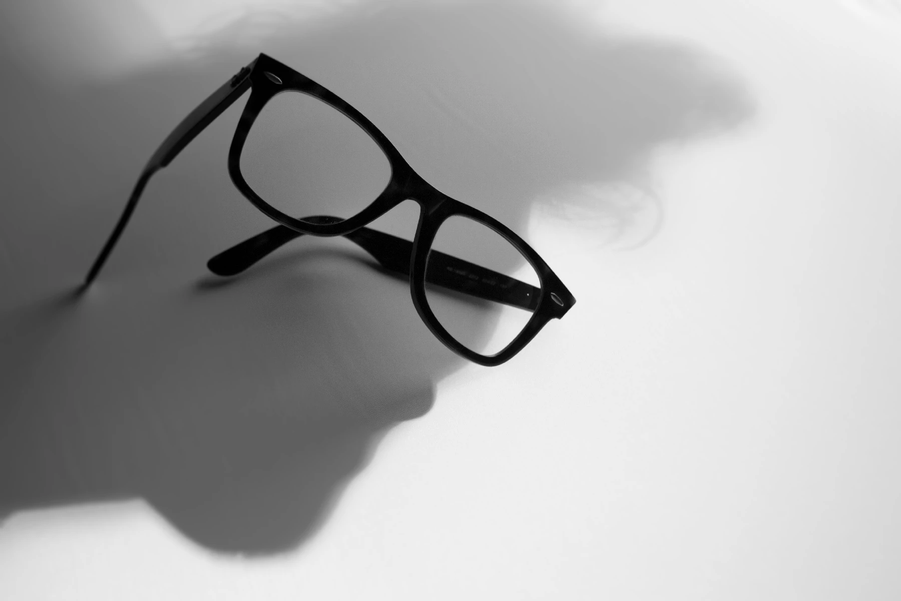 Photo of glasses with a silhouette of a face behind it.